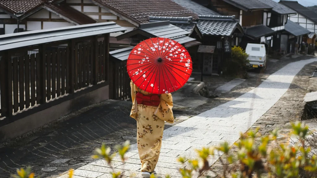 Seorang warga Jepang berjalan di permukiman tradisional dengan payung merah, ilustrasi kehidupan sehari-hari di tengah wacana penghapusan pajak makanan di Jepang